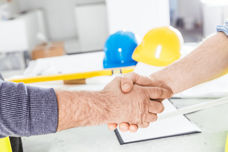 Partnerschaftliche Bauüberwachung: Handshake mit Helmen und Bauplänen